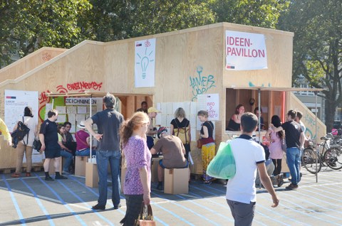 Das Bild zeigt einen Kiosk aus Holz mit vielen Menschen davor