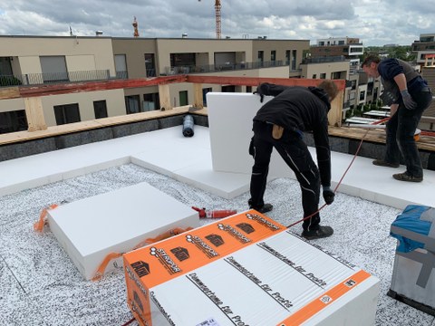 Two workmen lay insulation boards on a flat roof.