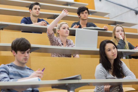 Eine Studentin sitzt in einem Hörsaal und meldet sich.