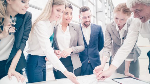 Eine Gruppe von Personen steht um einen Tisch herum und eine Frau zeigt auf einen Plan.