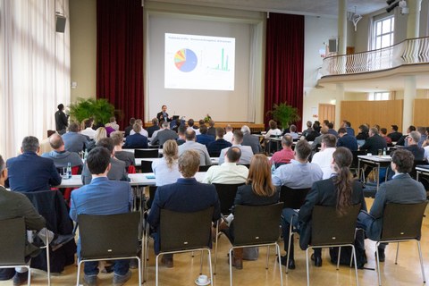 Teilnehmer, die den Vortragenden in einem Konferenzsaal zuhören.