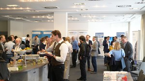 Ein Bild von vielen Menschen in einem großen Raum, die miteinander Reden, etwas essen und sich Ausstellungsstände von Firmen anschauen