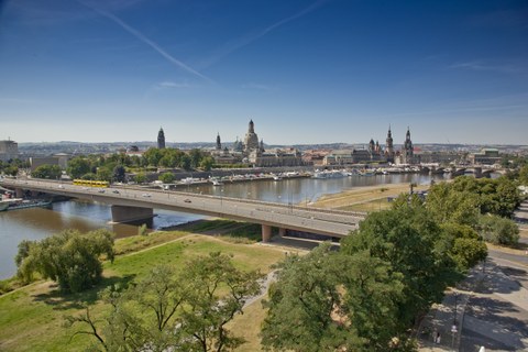 Photo shows the Carola Bridge in Dresden from an elevated position. In the background the city silhouette is visible.