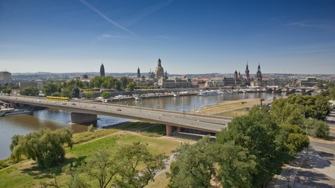 Photo shows the Carola Bridge in Dresden from an elevated position. In the background the city silhouette is visible.