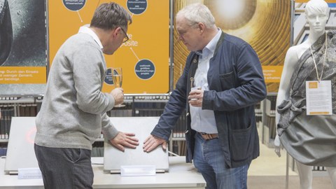Foto zeigt zwei Ausstellungsgäste bei der Begutachtung einer beheizbaren Carbonbeton-Platte