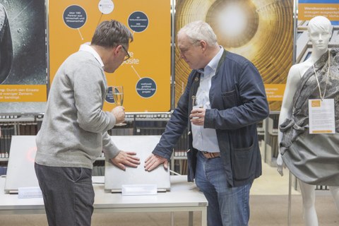 Photo shows two exhibition guests inspecting a heatable carbon reinforced concrete slab