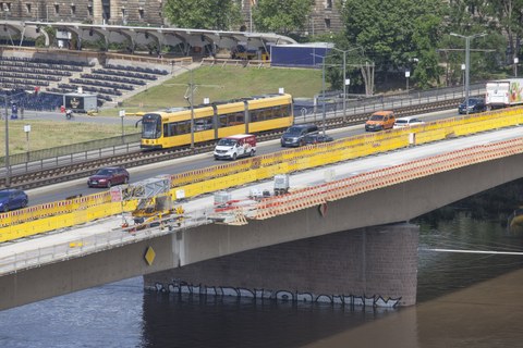 Foto zeigt einen Abschnitt der Carolabrücke während der Sanierung. Mehrere Autos und eine Straßenbahn überqueren die Brücke.