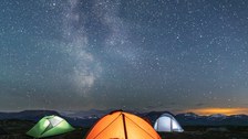 Foto zeigt drei beleuchtete Zelt und die Milchstraße bei Nacht