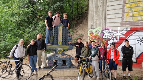 Group of students and lectorers with bicycles under a bridge