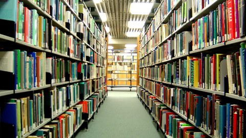 Foto zweier sich gegenüberstehender Regale, die mit Büchern gefüllt sind. In der Mitte ist ein Gang.