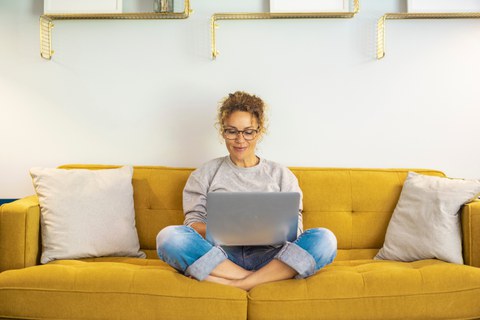 Frau sitzt mit Laptop auf dem Sofa