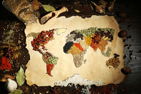 Das Foto zeigt einen Tisch mit vielen Gewürzen. In der Mitte des Tisches liegt ein Stück altes Papier mit den Umrissen einer Weltkarte. Die einzelnen Kontinente sind mit unterschiedlichen Gewürzen ausgefüllt. 