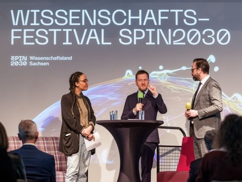 Moderatorin Ciani-Sophia Hoeder mit Ministerpräsident Kretschmer und Wissenschaftsminister Sebastian Gemkow im Gespräch auf einer Bühne bei der Eröffnungsveranstaltung Wissenschaftsfestival SPIN2030.