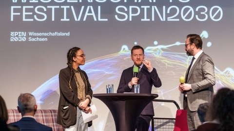 Moderatorin Ciani-Sophia Hoeder mit Ministerpräsident Kretschmer und Wissenschaftsminister Sebastian Gemkow im Gespräch auf einer Bühne bei der Eröffnungsveranstaltung Wissenschaftsfestival SPIN2030.