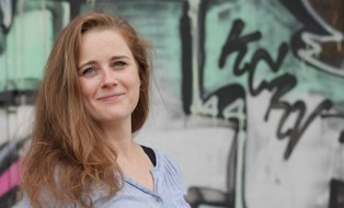 Auf dem Foto ist auf der linken Seite Aline Bergert im Profil zu sehen, der Hintergrund zeigt eine mit Street Art verzierte Wand.