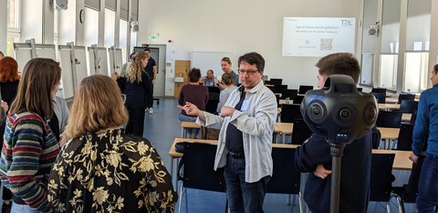Mehrere Personen stehen um eine 360-Grad-Kamera und hören der Erläuterung von Maik Jähne zu.