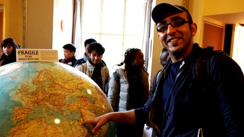 Humboldt fellow in front of a large globe labelled with a sign saying "fragile, please handle with care"