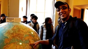 Humbodt Stipendiat vor einem großen Globus mit der Aufschrift "Zerbrechlich, bitte vorsichtig behandeln"