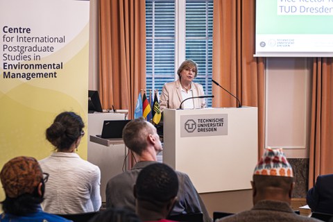Prof. Dr. Angela Rösen-Wolff spricht vor einer Gruppe von Zuhörer:innen, die im Vordergrund des Bildes zu sehen sind.