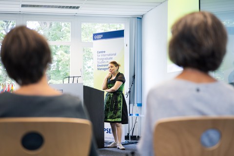 Prof. Dr. Angela Francke spricht begeistert bei SC92. Sie trägt ein grün-schwarzes bayerisches Dirndl, passend zur kulturellen Vielfalt, die einige Teilnehmende durch ihre Kleidung zeigen.