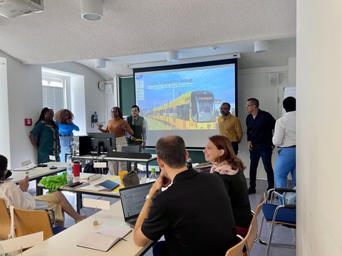 Foto im Seminarraum von CIPSEM: Die ÖPNV-Gruppe der Fallstudie Königsbrücker Straße steht oder sitzt zusammen und präsentiert ihre Ergebnisse auf einem Whiteboard oder Flipchart. Die Teilnehmenden lachen und lächeln—die Freude an der gemeinsamen Arbeit is