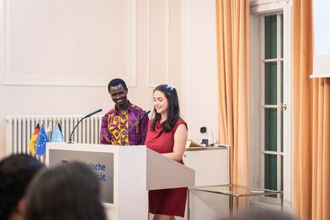 Zwei lächelnde EM49-Teilnehmende, Zibrina Salifu und Carolina Velásquez Arias, stehen hinter einem Rednerpult im Festsaal des Rektorats der TU Dresden.