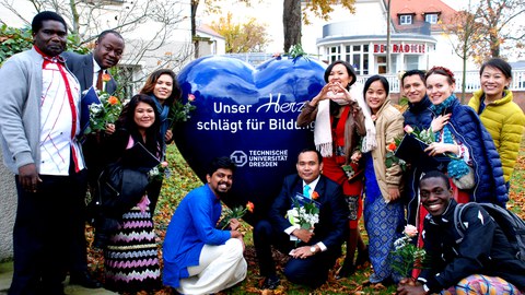 Image showing a group of course participants posing next to a large heart with "Our heart beats for education - TU Dresden" written on it.