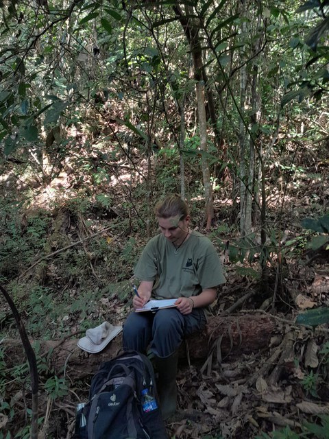 Kolja sitzt im Wald und schreibt in einem Notizbuch