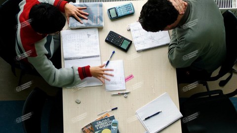 Zwei Studierende mit Taschenrechnern beugen sich über ihre Notizzettel.