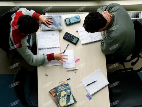 Zwei Studierende mit Taschenrechnern beugen sich über ihre Notizzettel.
