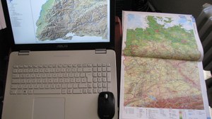 Das Bild zeigt eine Karte auf einem Notebook-Display und eine Atlaskarte