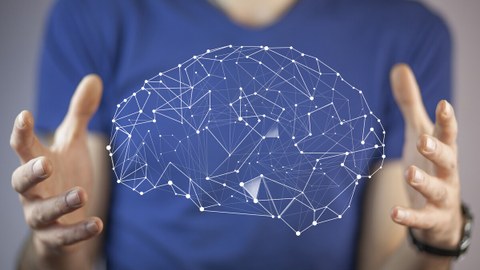 Das Bild zeigt den Oberkörper einer Person, die mit ihren Händen ein Hologramm eines Gehirnes präsentiert.