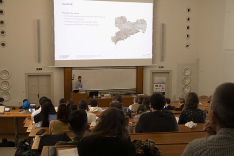 auditorium. A man stands in front and gives a presentation.