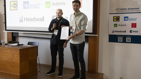 two person in front of a screen. One holding a certificate