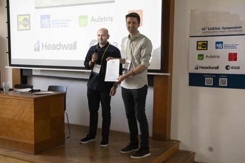 two person in front of a screen. One holding a certificate