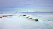 Blick über die durchs Eis stoßenden Felsen auf der Westseite der Bear Peninsula nach Süden zum ungefähr 70 bis 80 Kilometer entfernten Massiv des Mt. Murphy