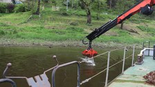 Eine Baggerschaufel entnimmt vom Schiff aus Proben vom Grund der Elbe