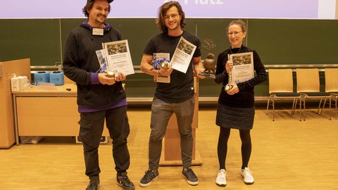 DGL-Nachwuchspreisträger präsentieren ihre Urkunden und Preise. Der 1. Preis (gehalten von C. Schwenk) ist eine Daphnienstatue. Abgebildet von links nach rechts: Johannes Feldbauer, C.  Schwenk, Lena Heinrich