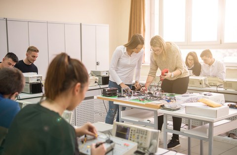 Bild von 8 Studenten, die in einem Klassenzimmer in zweier Gruppen zusammen an einem Elektroprojekt arbeiten.