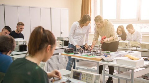 Bild von 8 Studenten, die in einem Klassenzimmer in zweier Gruppen zusammen an einem Elektroprojekt arbeiten.