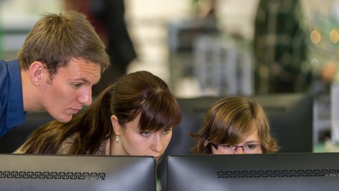 Zwei Studentinnen und ein Student schauen auf einen Bildschirm