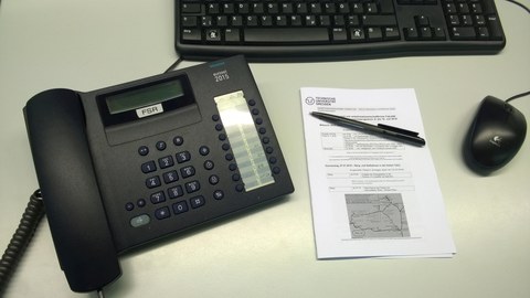 Telefon, Tastatur, Maus und Schreibblock liegen auf Schreibtisch.