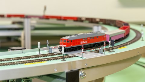 Modellbahnzug befährt einen Bahnübergang.