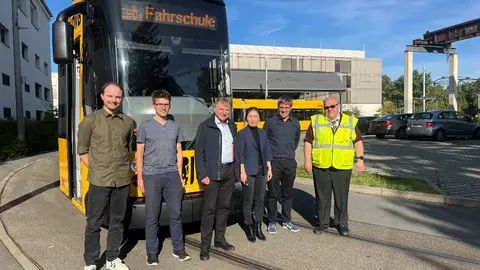 Sechs Personen, darunter Yihui Wang und Steffen Dutsch, stehen vor einer gelben Fahrschulstraßenbahn der Dresdner Verkehrsbetriebe.