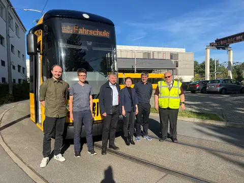 Sechs Personen, darunter Yihui Wang und Steffen Dutsch, stehen vor einer gelben Fahrschulstraßenbahn der Dresdner Verkehrsbetriebe.