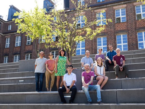 Das Team der Professur für Schienenfahrwege sitzend auf den großen Steinstufen vor dem Försterbau der TU Dresden. Alle schauen freundlich in die Kamera.
