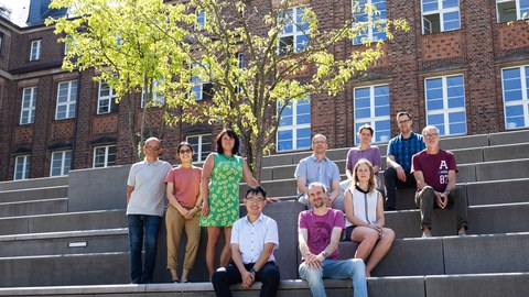 Das Team der Professur für Schienenfahrwege sitzend auf den großen Steinstufen vor dem Försterbau der TU Dresden. Alle schauen freundlich in die Kamera.