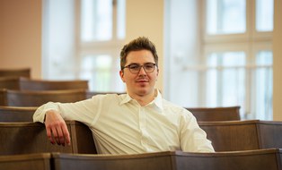 Dipl.-Ing. Aymeric Benken sitzt im Hörsaal und schaut in die Kamera