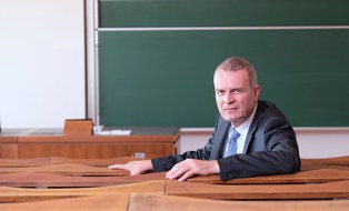 Herr Professor Lippold sitzt der Kamera zugewendet im Hörsaal vor der Tafel.