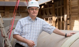 Torsten Seiler stützt sich auf einer Baustelle auf ein Beton-Wasserrohr und schaut in die Kamera.